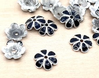 May include: A collection of silver flower-shaped metal beads with black enamel centres. Some beads are plain silver, while others have a black enamel design.