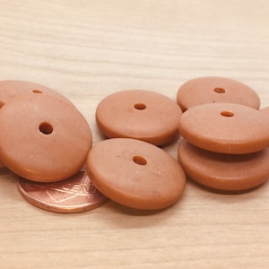 May include: A group of six brown wooden beads with a hole in the center. The beads are arranged in a pile on a wooden surface.