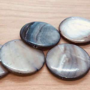 May include: Six round, flat, white and gray mother of pearl shell beads with a hole drilled through the center.