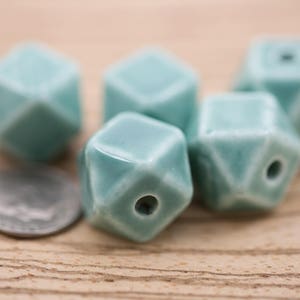 May include: Five teal blue ceramic beads with a geometric shape. Each bead has a hole in the center for stringing.