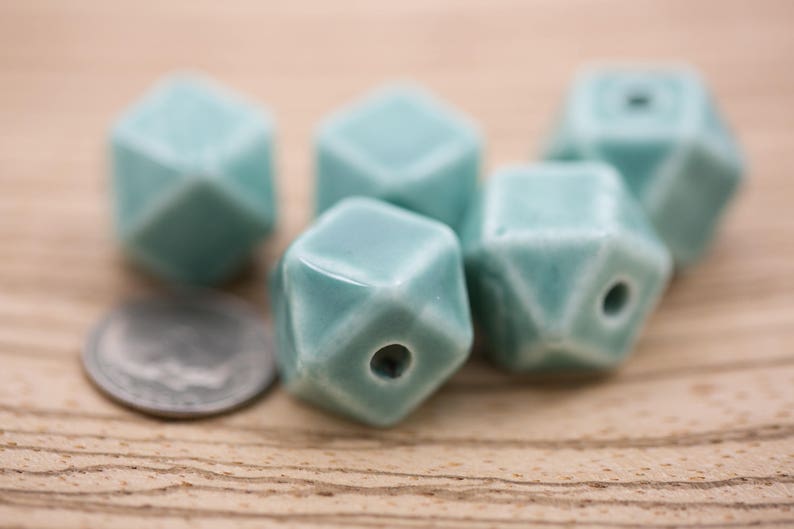 May include: Five teal blue ceramic beads with a geometric shape. Each bead has a hole in the center for stringing.