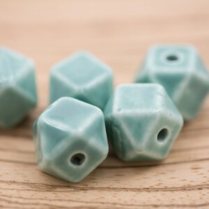 May include: Five teal blue ceramic beads with a geometric shape. Each bead has a hole in the center.