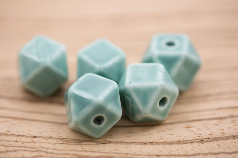 May include: Five teal blue ceramic beads with a geometric shape. Each bead has a hole in the center.