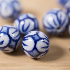 May include: A close-up of blue and white ceramic beads with a floral pattern. The beads are scattered on a wooden surface.