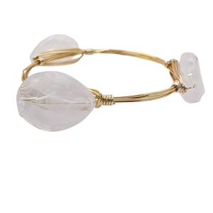 May include: A gold wire wrapped bracelet with three clear quartz stones. The stones are faceted and have a natural, organic shape.