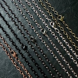May include: A variety of chain styles in different metal finishes, including silver, gold, black, and copper. The chains are laid out in parallel lines on a dark surface.