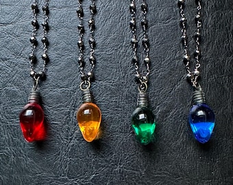May include: Four necklaces with light bulb pendants. The necklaces are made of black beads and the light bulbs are red, orange, green, and blue.