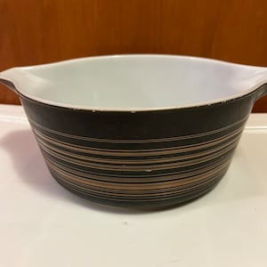 May include: A black and gold striped mixing bowl with a white interior. The bowl has a rounded shape and two handles.