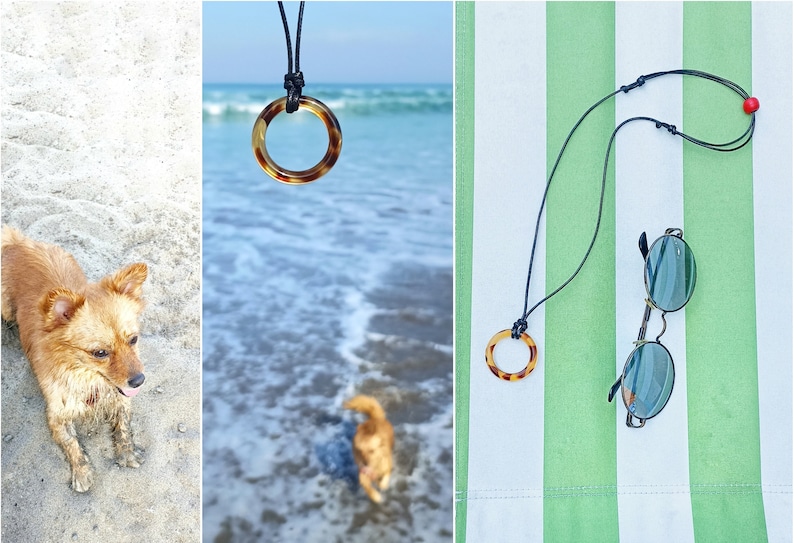 May include: A black leather cord necklace with a brown tortoiseshell ring pendant. The necklace is lying on a green and white striped beach towel with a pair of round sunglasses.