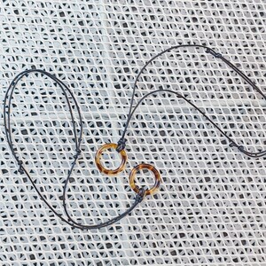 May include: A black cord necklace with two tortoiseshell pendant rings. The necklace has a red bead at the end.