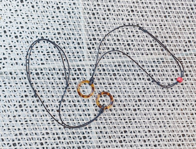 May include: A black cord necklace with two tortoiseshell pendant rings. The necklace has a red bead at the end.