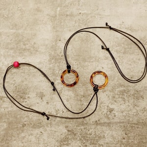 May include: Two brown tortoiseshell rings on black cords with a pink bead on one cord.