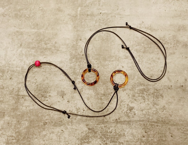 May include: Two brown tortoiseshell rings on black cords with a pink bead on one cord.