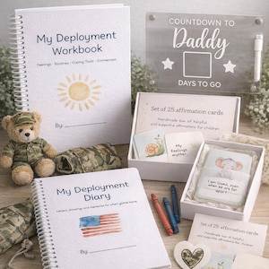 May include: A collection of items for deployment support, including a spiral-bound "My Deployment Workbook" and "My Deployment Diary", affirmation cards, a countdown sign, and a teddy bear in a military uniform. The items are arranged on a wooden surface.