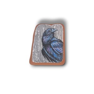 May include: A hand-painted raven illustration on a rectangular, brown-edged ceramic tile. The raven is depicted in shades of black and blue against a gray and white background. The artwork has a rustic, artistic style.