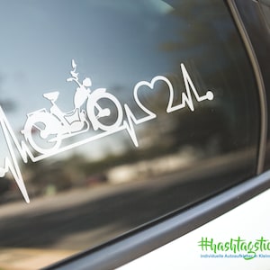 May include: White vinyl decal of a moped with a heart and a heartbeat line. The decal is on a car window. The text on the bottom of the image is "#hashtagticker.de individuelle Autoaufkleber in Kleinauflage".