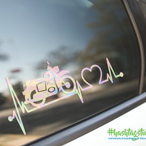 Könnte beinhalten: Ein regenbogenfarbener, schimmernder Vinyl-Aufkleber mit einem Traktor, einer Herzschlaglinie und dem Text "#hashtagticker.de" und "individuelle Autoaufkleber in Kleinauflage".