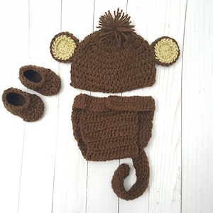 May include: A brown crocheted monkey costume for a baby, including a hat with ears, a diaper cover, and booties.