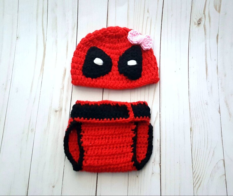 May include: Red and black crocheted baby hat and diaper cover with a black eye mask and a pink bow on the hat.
