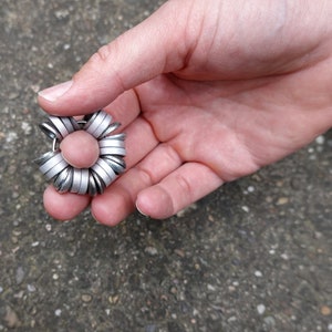May include: A silver metal ring made of many smaller rings stacked together in a flower shape.
