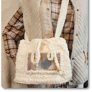 Può includere: Una borsa bianca all'uncinetto con una finestra a rete e una chiusura con coulisse. La borsa è indossata sopra una camicia a quadri marrone e bianca e un gilet trapuntato color crema. Il testo "Crochet Some Fun with Jeannie Wilburn" è visibile nell'angolo in alto a sinistra dell'immagine.