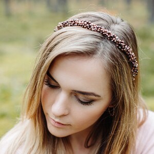 Può includere: Una donna con lunghi capelli biondi indossa un maglione rosa e una fascia per capelli con perline. La fascia è fatta di piccole perline marroni e dorate.