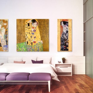 Puede incluir: Tres pinturas enmarcadas de obras de arte famosas de Gustav Klimt. Las pinturas est&aacute;n colgadas en una pared blanca sobre una cama con ropa de cama blanca y un piecero morado. Las pinturas son todas en un estilo similar, con acentos dorados y negros.