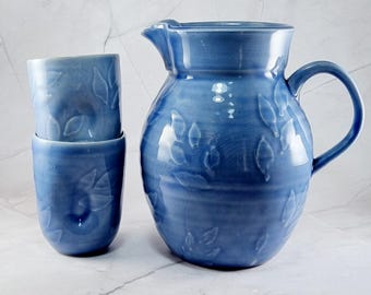set van blauwe kan en twee kopjes versierd met bladeren handgemaakt keramiek
