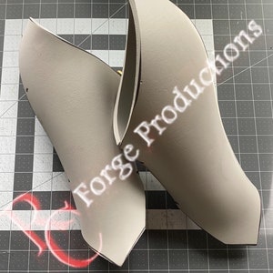 Puede incluir: Dos piezas de espuma grises, posiblemente para cosplay o la elaboración de disfraces, con el texto "Forge Productions" impreso en una pieza.