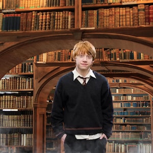 May include: A young person with red hair is standing in a library. The person is wearing a black sweater with a red stripe, a white shirt, and black pants. The person is looking at the camera. The text "When in doubt, go to the library." is displayed above the person.