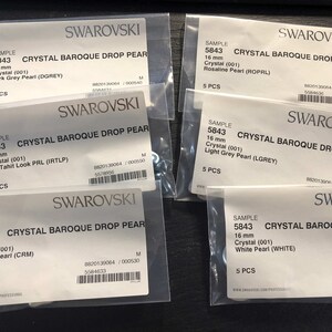 Op de afbeelding: Vijf doorzichtige plastic zakjes, elk met vijf kristallen barokke druppelvormige parels. De zakjes zijn voorzien van het Swarovski-logo en productinformatie, waaronder de parelmaat, kleur en code. De parels zijn 16 mm groot en verkrijgbaar in verschillende kleuren, waaronder donkergrijs, lichtgrijs, crème, wit en rosaline.