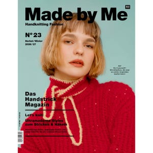 Könnte beinhalten: Das Cover des Magazins Made by Me Handknitting Fashion Nr. 23 Herbst/Winter 2026/27 zeigt eine Person mit kurzem blonden Haar, die einen leuchtend roten, strukturierten Pullover mit einem cremefarbenen Häkelschal um den Hals vor blauem Hintergrund trägt.