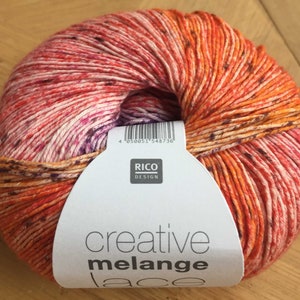 Könnte beinhalten: Eine Knäuel orangefarbenes, rosafarbenes und weißes Garn mit einem weißen Etikett, auf dem "creative melange lace" und "RICO DESIGN" steht.