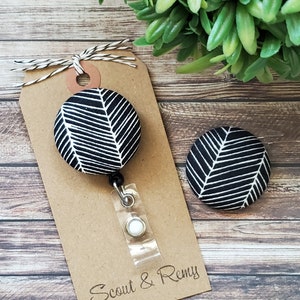 May include: Black and white patterned fabric badge reel with a white button and a brown tag that says "Scout & Remy".