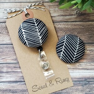 May include: Black and white patterned fabric badge reel with a clear plastic retractable cord and a silver clip. The badge reel is attached to a brown card with the text "Scout & Remy" printed on it.