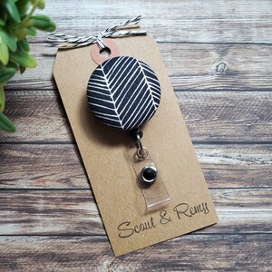 May include: Black and white patterned fabric badge reel with a clear plastic badge holder and a black metal clip. The badge reel is attached to a brown card with the text "Scout & Remy".