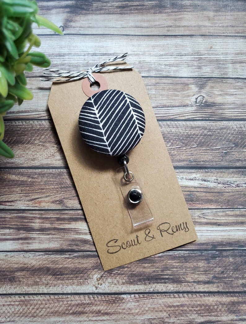 May include: Black and white patterned fabric badge reel with a clear plastic badge holder and a black metal clip. The badge reel is attached to a brown card with the text "Scout & Remy".