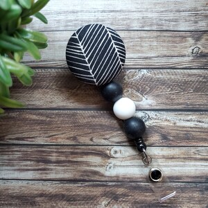 May include: Black and white patterned fabric badge reel with black and white beads. The badge reel has a clear plastic strap and a metal clip.