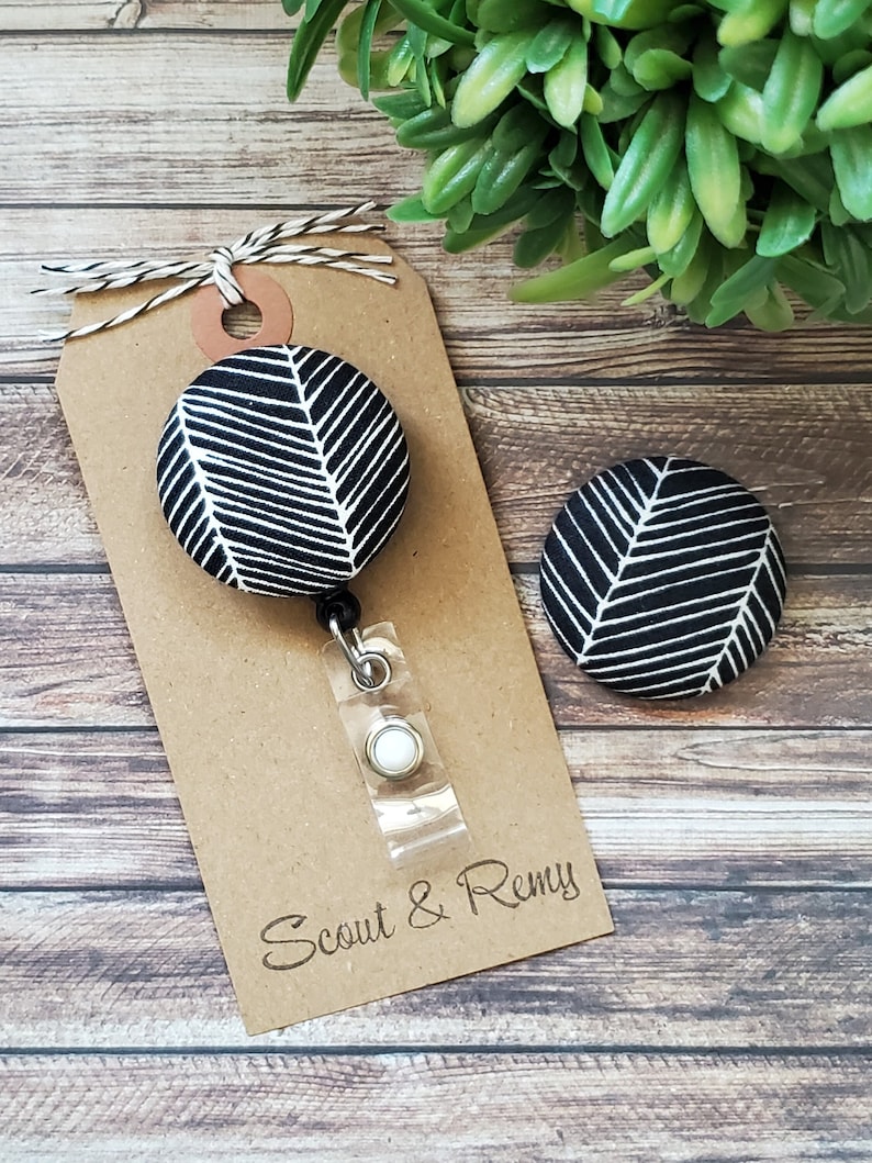May include: Black and white patterned fabric badge reel with a white button and a brown tag that says "Scout & Remy".