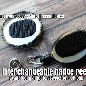 May include: Interchangeable badge reel with a black and white patterned fabric cover. The reel has a black retractable cord and a black alligator clip. The text "change out your covers for different looks!" and "interchangeable badge reel available in alligator swivel or belt clip" is visible in the image.