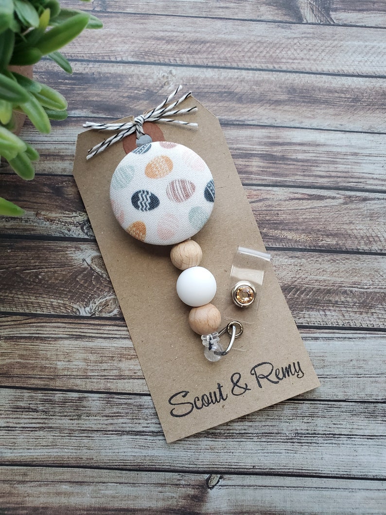 May include: A brown card with the text "Scout & Remy" printed on it. A white and brown beaded retractable badge holder with a fabric button featuring a white background with colorful polka dots.