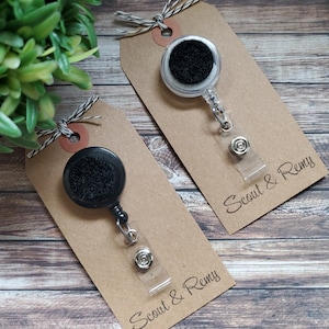 May include: Two black retractable badge holders with clear plastic straps and black felt circles. The holders are packaged on brown cardstock tags with the text "Scout & Remy" printed on each tag.