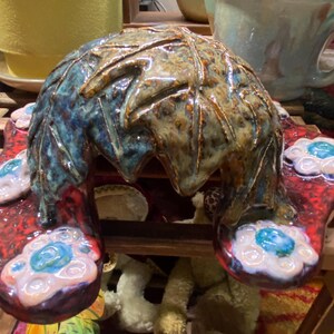 May include: A ceramic sculpture of a leafy archway with a red and white base. The archway is decorated with blue and white flowers.