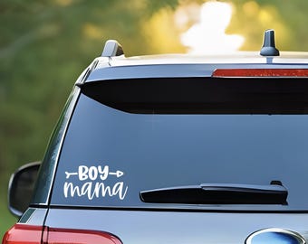 May include: A white vinyl decal with the text "Boy Mama" and an arrow on either side, attached to the rear window of a silver car.
