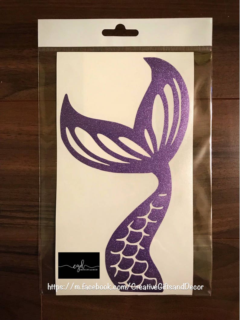 May include: A purple glitter mermaid tail decal inside a clear plastic sleeve. The decal features a cutout scale pattern on the tail and a fin design. A black rectangular logo with the text cgd and the URL https://m.facebook.com/CreativeGiftsandDecor is visible at the bottom.