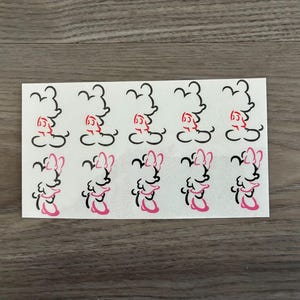 May include: A sheet of white stickers featuring cartoon character outlines. The top row has black and red images, while the bottom row has black and pink images. The stickers are arranged in a grid pattern on a white rectangular sheet.
