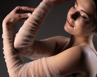 May include: A woman wearing a white dress with sheer, sparkly, long sleeves. The sleeves are gathered at the wrist.