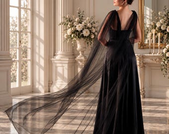 May include: A floor-length black gown featuring a sleeveless bodice with a deep V-neckline and a long, flowing sheer tulle cape attached at the shoulders that extends behind the garment, creating a dramatic silhouette with a smooth satin skirt.