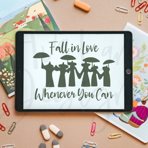 Könnte beinhalten: Ein schwarzes Tablet zeigt den Text "Fall in Love Whenever You Can" über einer Silhouette von Figuren mit Regenschirmen. Das Tablet ist von Schreibwaren umgeben, darunter Notizbücher und Büroklammern.