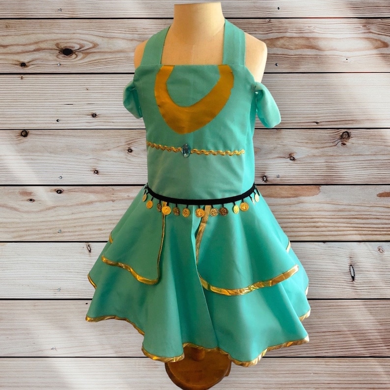 May include: A turquoise dress with gold trim and a gold crescent moon design on the bodice. The dress has a black belt with gold coins and a layered skirt.
